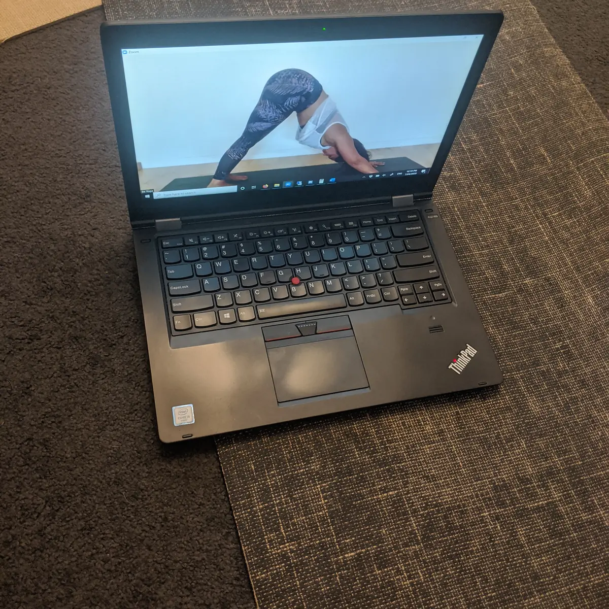 A laptop on a carpeted floor showing an online yoga class over video call