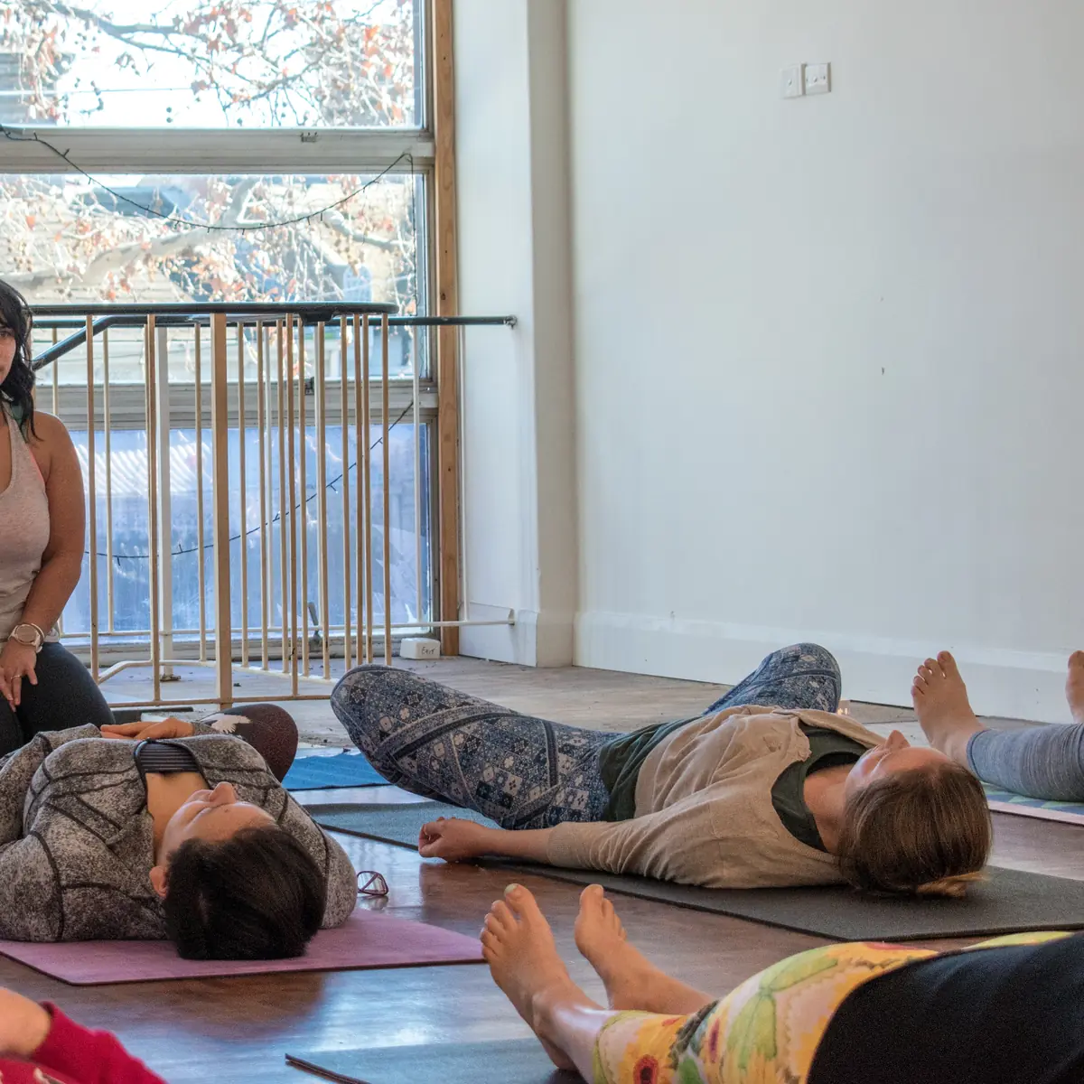 Students resting in savasana on mats in a sunlit studio